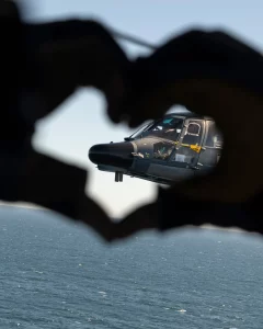 Silhouette de mains formant un cœur laissant voir un hélicoptère au-dessus de la mer en PACA, photographie artistique d’une vidéaste professionnelle.